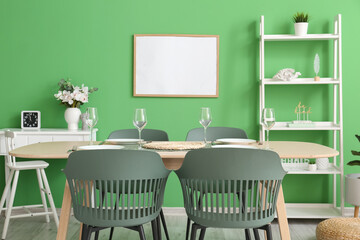 Interior of stylish dining room with tables, shelving unit and green wall