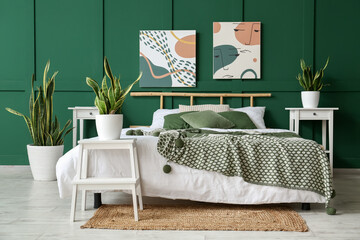 Interior of stylish bedroom with paintings, houseplants and green wall