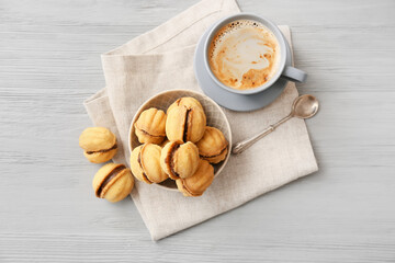 Bowl of tasty walnut shaped cookies with condensed milk and cup of coffee on table