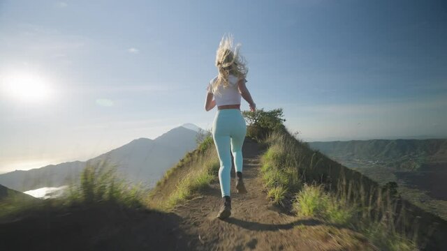 Dauntless young female running on mountain edge of mount Batur at sunrise