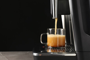 Modern espresso machine pouring coffee into glass cup on grey table against black background. Space...