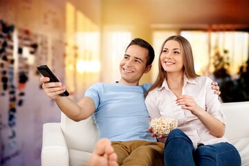 Young cheerful couple eating popcorn and watches a movie on TV with the remote control