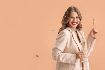 Beautiful young woman with Christmas sparkler and champagne on beige background