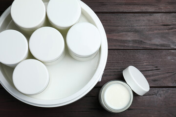 Modern yogurt maker with full jars on wooden table, flat lay