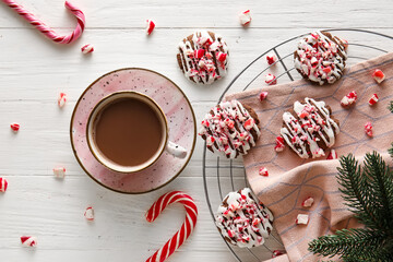 Grid with tasty candy cane cookies and cup of coffee on white wooden background