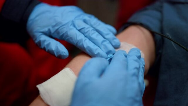 Closeup paramedic fixing medical plaster on man hand with catheter in vein