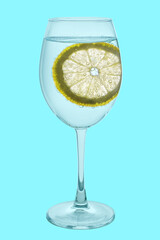 Carbonated, clear water in a glass goblet with a round slice of yellow lemon in air bubbles. Isolated on a light blue background. Close-up.