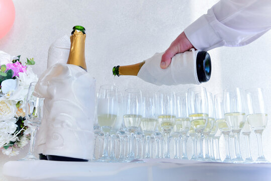 Close up of a male hand pouring a bottle of champagne on glass cups on a white table