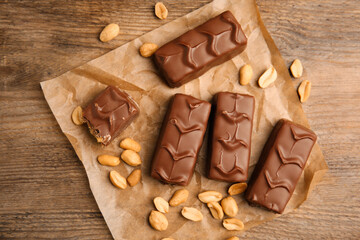 Chocolate bars with nuts and parchment on wooden table, flat lay