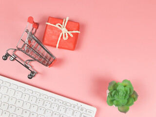 flat lay of  computer keyboard shopping cart or trolley, red gift box  and succulent in plant pot on pink background with copy space. Holiday shopping online concept.