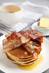 Delicious pancakes with maple syrup and fried bacon on plate, closeup