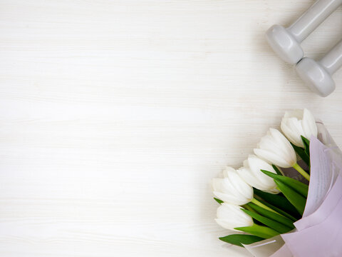 Two white dumbbells and tulips on white background with copyspace. Healthy fitness lifestyle flat lay composition for Valentine's Day, birthday, anniversary or wedding.