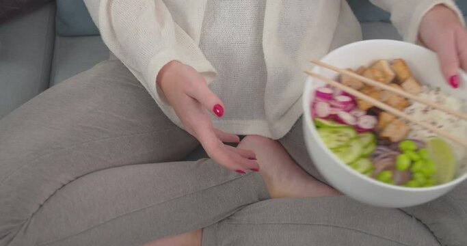 A woman sitting cross-legged in the sofa while having her meal. close up view