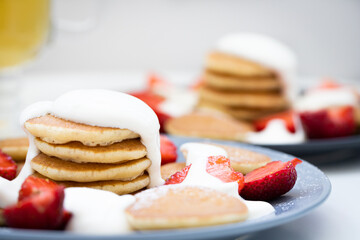 Mini pancakes with sour cream sauce and strawberries on plates, breakfast for the family. Front view.