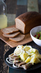 Homemade rye bread in slices with a plate of potatoes and herring. Salad and booze. Front view.