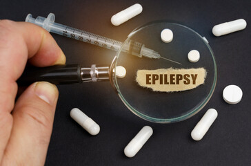A man looks through a magnifying glass at pills, a syringe and a piece of paper with the...