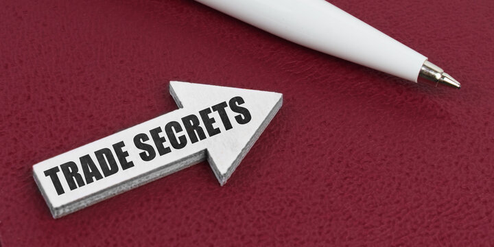 On a red background lies a white pen and a white arrow with the inscription - TRADE SECRETS - Powered by Adobe