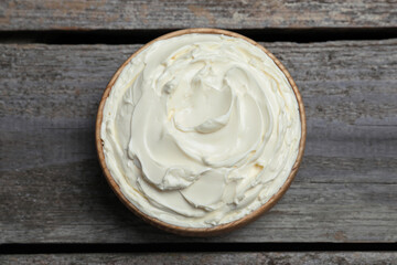 Bowl of tasty cream cheese on wooden table, top view