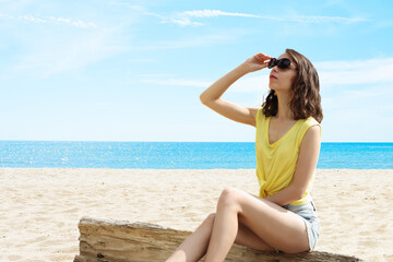Fototapeta na wymiar Girl on the beach in sunglasses looks into the sky. The concept of relaxation, vacation, pleasure.
