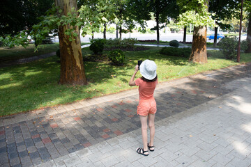 Girl child tourist photographs trees in the park on a smartphone. Travel to another country.