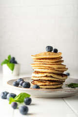 sweet pancakes for breakfast in a stack. on a ceramic plate. with fresh blueberries and mint. light key vertical position