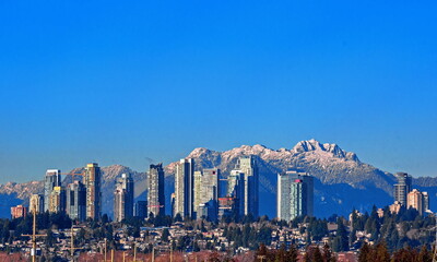 New residential area of  high-rise buildings in the city of Burnaby, construction site in the center of the city against the backdrop of snow covered mountain range and blue sky