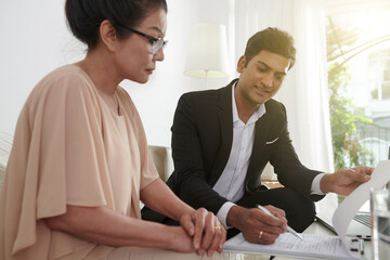 Insurance agent showing senior woman where to sign life insurance policy document