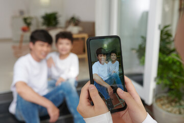 Hands of teenage boy photographing father and his preteen son on smartphone