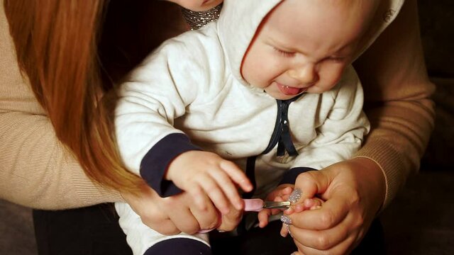 Mother trims her daughter toenails. Child is upset