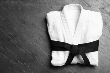 Martial arts uniform with black belt on grey stone background, top view. Space for text - obrazy, fototapety, plakaty