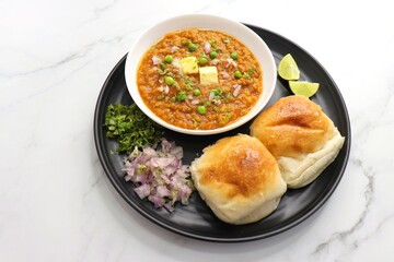  Indian Mumbai Street style Pav Bhaji, garnished with peas, raw onions, coriander, and Butter. Spicy thick curry made of out mixed vegetables served with pav over white background with copy space.