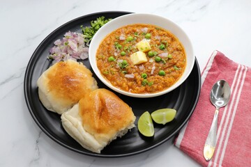  Indian Mumbai Street style Pav Bhaji, garnished with peas, raw onions, coriander, and Butter. Spicy thick curry made of out mixed vegetables served with pav over white background with copy space.