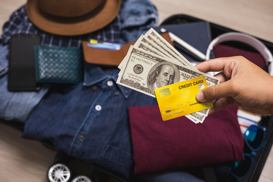 Close up traveler hand man showing credit card and cash payment for travel. Trolley bag and Travel accessories on the background. Reward point for travelling. Loyalty card program for tourist