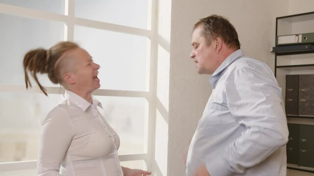 Conflict disagreement between businessman and businesswoman or employees at work in office. Man and woman shout at each other, argue and swear.