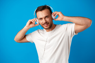 Young man listening to music with headphones on blue background.