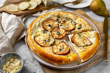 Homemade puff pastry pizza with pear, almonds, ricotta gorgonzola or blue cheese on the kitchen table. Delicious layered pie with pear, dorblu, nuts on a light culinary background