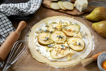 The process of cooking puff pastry pizza with pear, almonds, ricotta gorgonzola or blue cheese on a culinary background. Raw ingredients for layer cake with pear, dorblu, nuts on the table