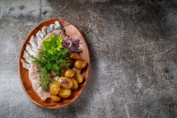 Serving a dish from a restaurant menu. Salted sliced herring fish with pickled mushrooms and onions, cream sauce, dill and parsley greens on a plate against the background of a gray stone table