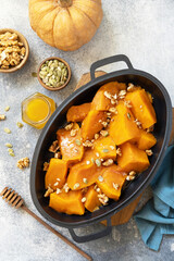Healthy dessert or vegan lunch. Baked pumpkin. Delicious baked sweet pumpkin with nuts, pumpkin seeds and honey over gray stone background. Top view flat lay.