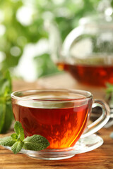Glass cup of aromatic black tea with fresh mint on wooden table against blurred background. Space for text