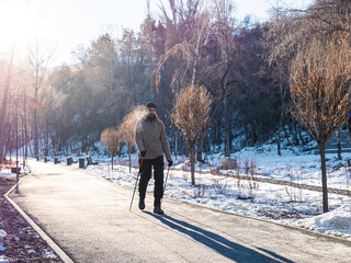 A bearded man is engaged in scandinavian walking, in a winter park in an early frosty morning....