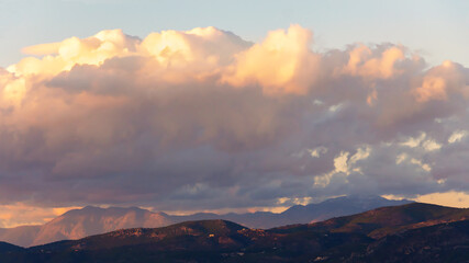 Beautiful fluffy clouds over the mountains on sunny day at golden hour painted with sun