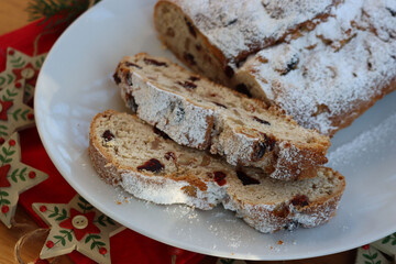 Traditional german sweet bread with raisins and candied fruits called Stollen on a plate on wooden table with festive Christmas decorations