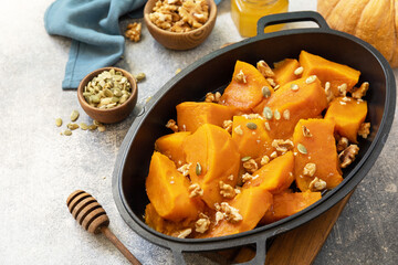 Healthy dessert or vegan lunch. Baked pumpkin. Delicious baked sweet pumpkin with nuts, pumpkin seeds and honey over gray stone background. Copy space.