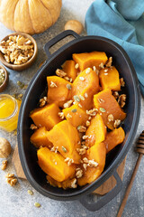 Healthy dessert or vegan lunch. Baked pumpkin. Delicious baked sweet pumpkin with nuts, pumpkin seeds and honey over gray stone background.