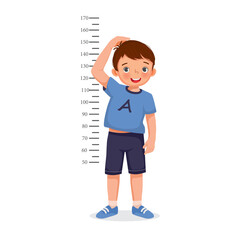 Cute Little boy measuring height of his growth on the background of wall - obrazy, fototapety, plakaty