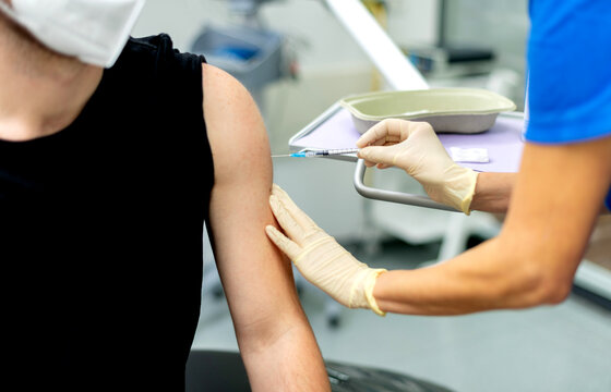 Booster  Impfung in der Zahnarztpraxis, Spritze am Oberarm eines Erwachsenen.