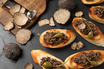 Tasty bruschettas with truffle paste and capers on black table, flat lay