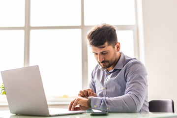 Fototapeta premium Portrait of businessman sitting at office while looking at his watch. Young professional getting ready for business meeting.