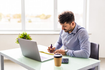 Fototapeta premium Entrepreneur writing notes sitting at his desk. Young man making business plans with papers and computers on his desk in office.